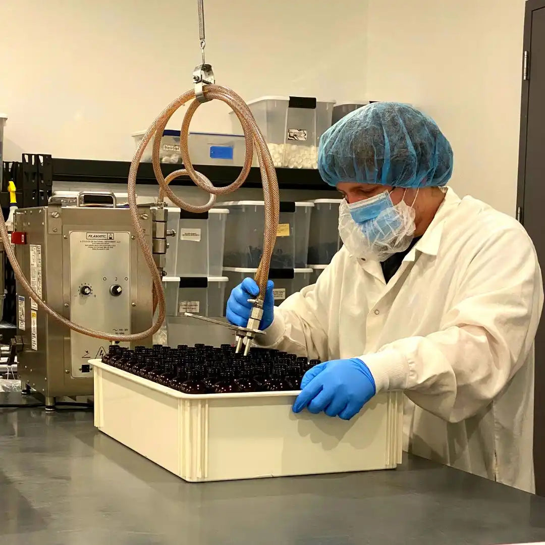 Laboratory technician in protective gear filling vials with liquid.