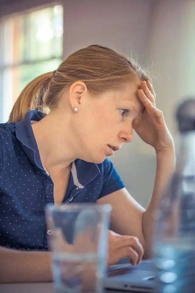 Someone appearing stressed or worried while sitting at a desk with a glass of water.